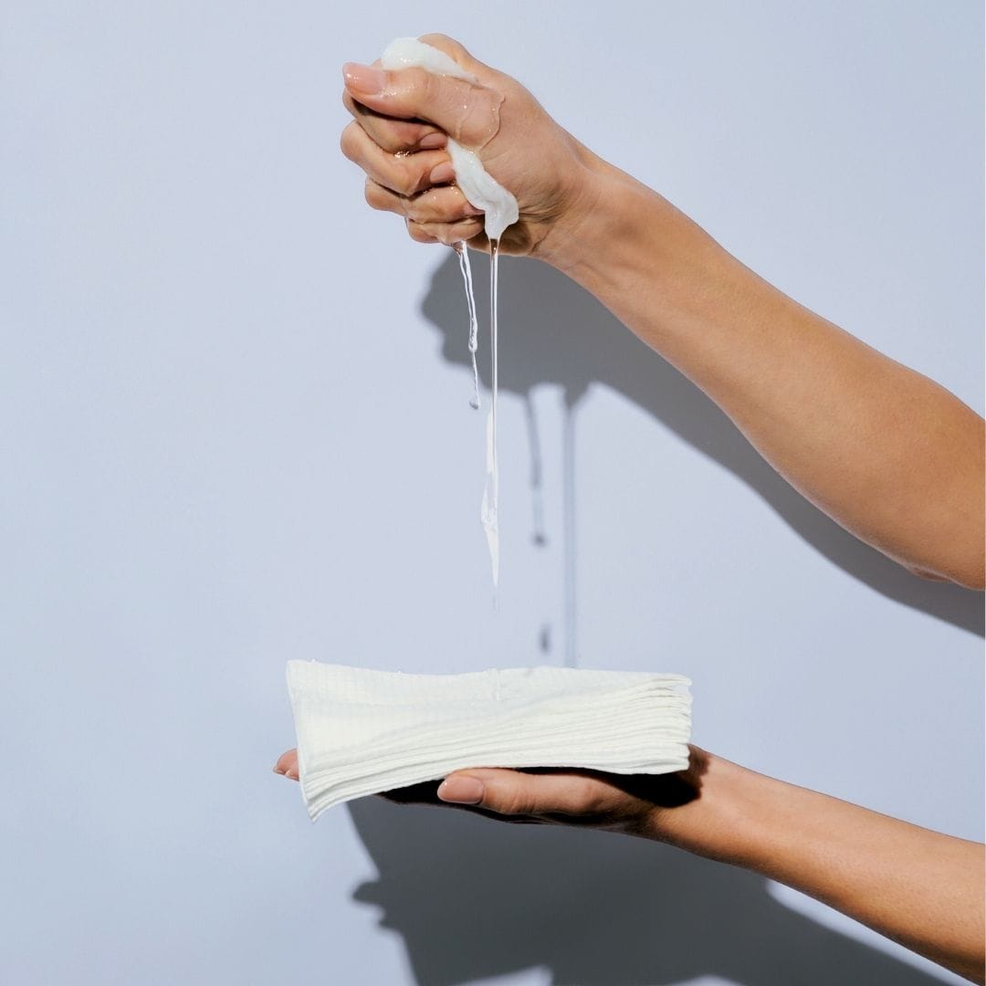 Hand holding a stack of white paper cloths against a light blue background