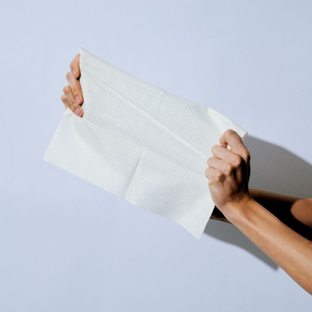Person holding a white textured cleansing cloth against a light blue background